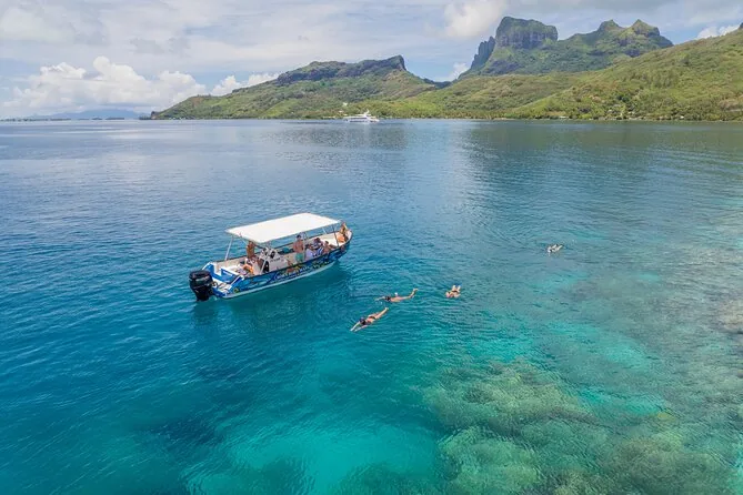 A small tour boat on the turquoise lagoon below Mount Otemanu